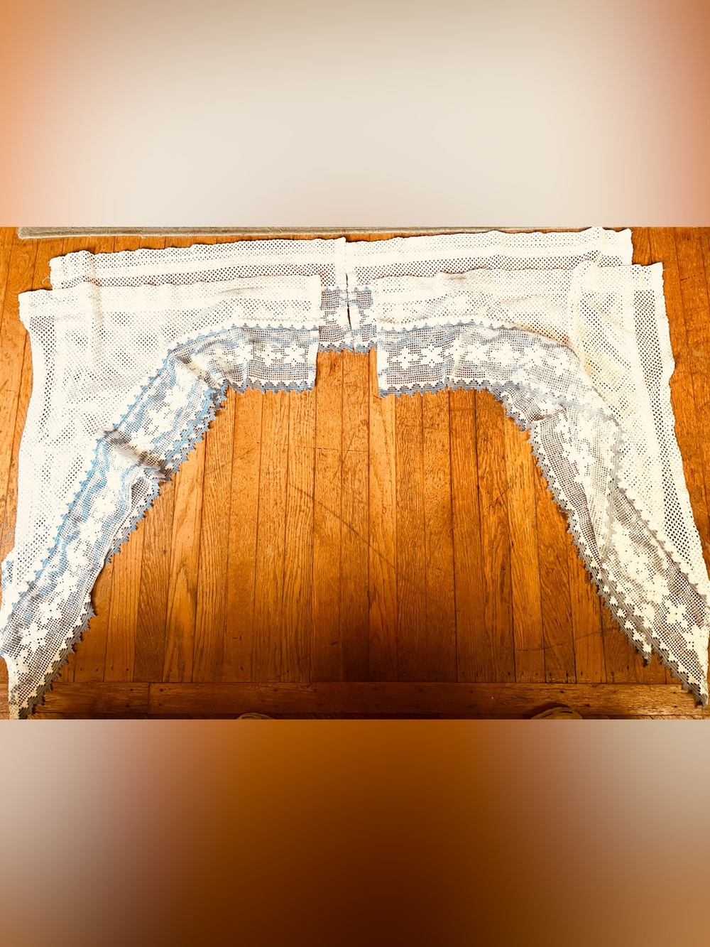 Two pairs of open weave curtains with a blue and white scalloped floral trim.